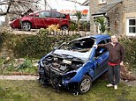 Steve Cobbin stands next to a car that landed in his garden after leaving the road and crashing into his neighbour Colin Brine's car in the background 
