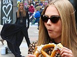 Keep the carbs coming! Cara Delevingne scoffs a giant pretzel as she continues shooting for her DKNY campaign